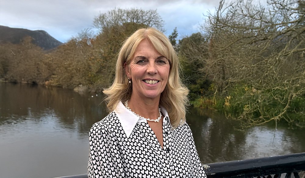 Close up of a woman standing on a bridge with a river and countryside in the background